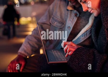 Close-up of young couple using laptop in the city at night Stock Photo