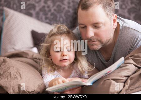 Father and daughter reading a book in bed Stock Photo