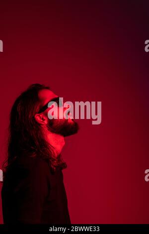 Profile of red illuminated young man wearing sun glasses against red background Stock Photo