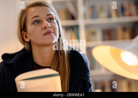 Portrait of thoughtful young woman with a book at home Stock Photo