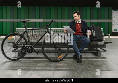 Businessman with bicycle reading documents while sitting at subway station platform, Frankfurt, Germany Stock Photo