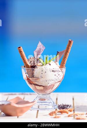 Closeup of glass bowl with mint, vanilla ice cream scoops on blur bokeh background with copy space. Waffle chocolate rolls on white table top of blue Stock Photo