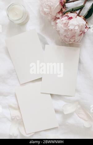 Wedding stationery, still life composition. Greeting cards mockup scene. Blank sheets of paper and pink peony flowers on white linen table cloth Stock Photo