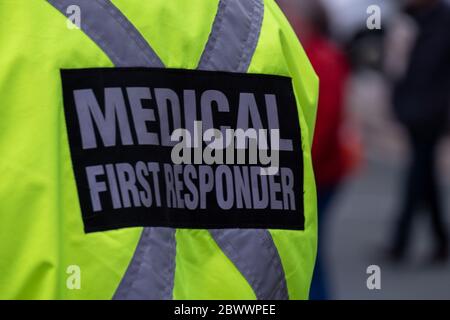 A bright yellow medical first responder uniform being worn by a large male in a crowded street.The coat has a grey reflective cross across the back. Stock Photo