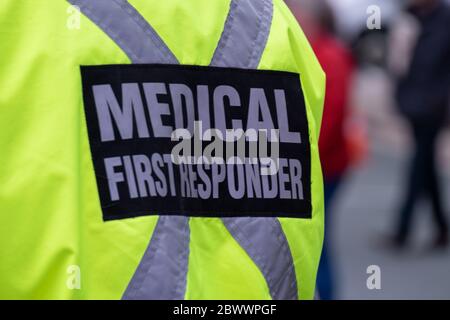 A bright yellow medical first responder uniform being worn by a large male in a crowded street.The coat has a grey reflective cross across the back. Stock Photo