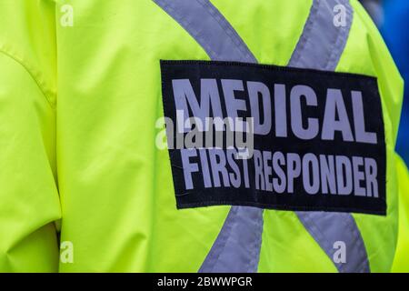 A bright yellow medical first responder uniform being worn by a large male in a crowded street.The coat has a grey reflective cross across the back. Stock Photo