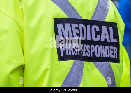 A bright yellow medical first responder uniform being worn by a large male in a crowded street.The coat has a grey reflective cross across the back. Stock Photo