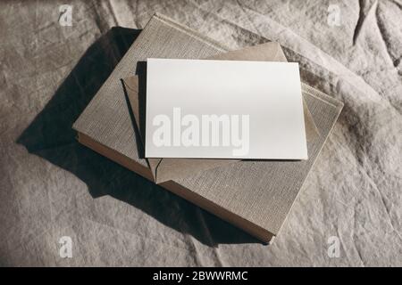 Moody stationery still life scene. Old book, blank sheet of paper, greeting card mockup and envelope in sunlight. Beige linen tablecloth background Stock Photo