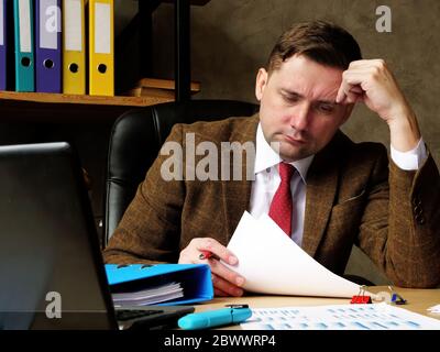 Serious tired accountant reads and works with financial statements. Stock Photo
