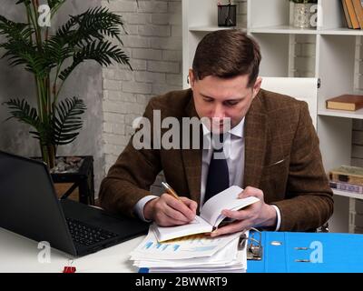 Man in suit making notes while working with financial charts and statements in office. Stock Photo
