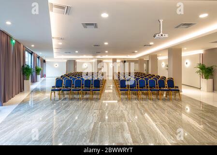 Rows of vintage blue chairs on beige glossy marble floor in modern light hall interior of luxury office building. Auditorium background with copy spac Stock Photo