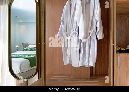 Front view of wooden wardrobe cabinet with mirror and hanging white bathrobe in modern hotel room interior Stock Photo