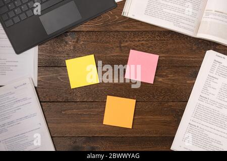 Open books, colored stickers and laptop on wooden desk background, flat lay Stock Photo