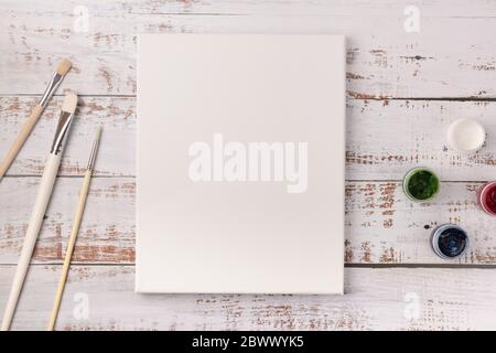 Colorful creative table with blank canvas for sketches and paints, paintbrushes set on white wooden table Stock Photo