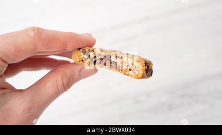 Bitten chocolate chip cookie in hand. Hand holding cookie with chocolate drops on white wooden background Stock Photo