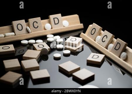 OCD concept spelled in text with pharmaceutical medication on a black table. Obsessive Compulsive Disorder and behavioral health issues. Stock Photo