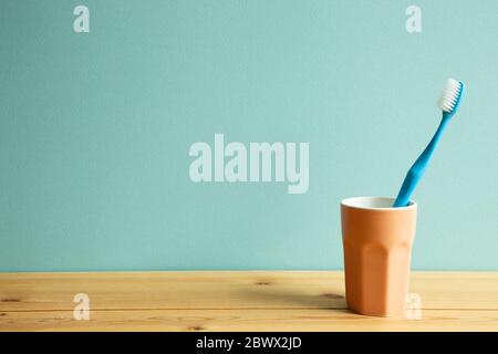 Blue toothbrush in cup on wooden table with mint background. copy space Stock Photo