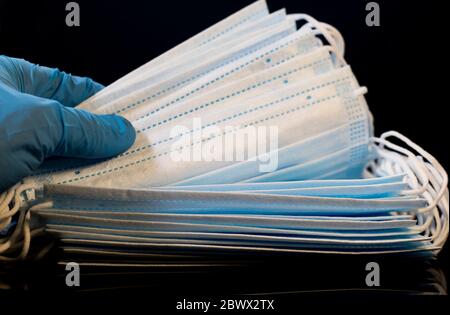 Surgical masks counted by gloved hand. Medical and health care concept. Close up face masks used in hospitals by nurses and doctors. Medical respirato Stock Photo