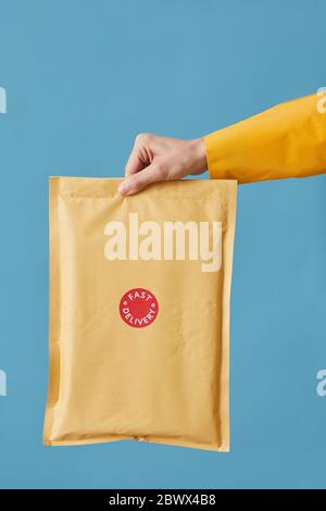 Close-up of postman holding parcel packed in paper isolated on blue background Stock Photo