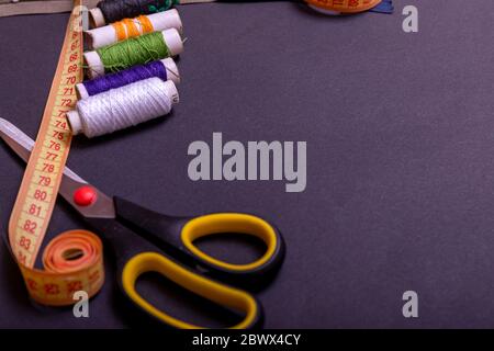 Copyspace frame with sewing tools and accesories. Tools for sewing and handmade: thread, scissors, pins on black paper. Stock Photo
