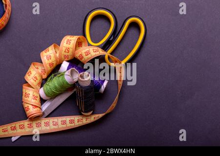 Copyspace frame with sewing tools and accesories. Tools for sewing and handmade: thread, scissors, pins on black paper. Stock Photo
