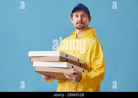 Portrait of young man in uniform holding pizza boxes and looking at camera against the blue background he delivering pizza Stock Photo
