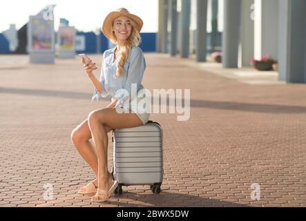 Female tourist sitting on baggage near airport terminal Stock Photo
