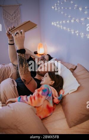 vertical image of father laying in bed reading to kids Stock Photo