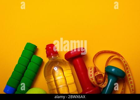 Fitness and diet concept background. Tennis ball with dumbbells and bottle of water isolated on yellow background. Top view with copy space. Stock Photo