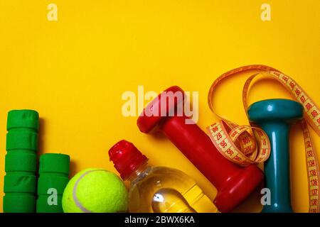Fitness and diet concept background. Tennis ball with dumbbells and bottle of water isolated on yellow background. Top view with copy space. Stock Photo