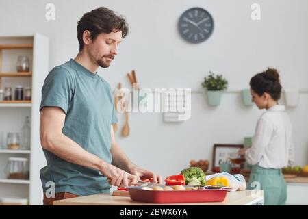 Young man cutting vegetables for dinner he helping his wife in the kitchen at home Stock Photo