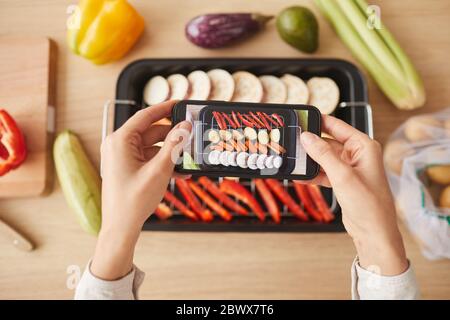 High angle view of woman holding mobile phone and photographing her prepared dish from vegetables Stock Photo