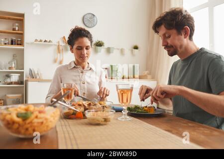 Young couple sitting at the table and enjoying dinner together in domestic kitchen Stock Photo