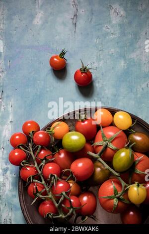 Colourful tomatoes on a pewter plate over old, painted wood background Stock Photo
