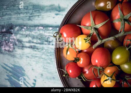 Colourful tomatoes on a pewter plate over old, painted wood background Stock Photo
