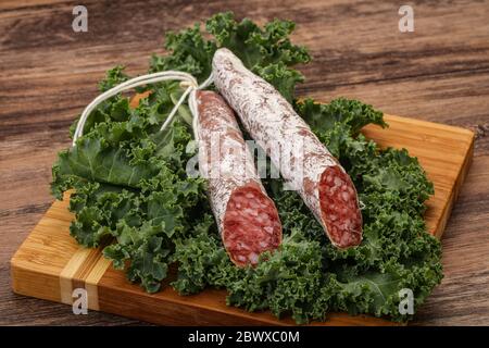 Spanish Fuet sausage with salad leaves over wooden background Stock Photo