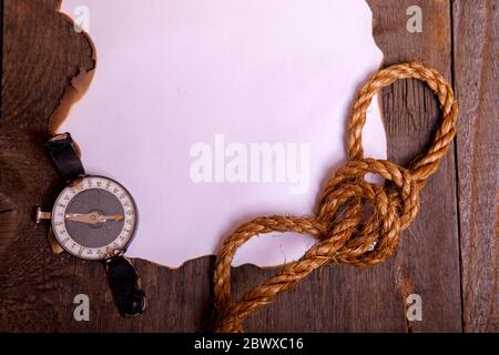 Old paper with compass, knife and rope on vintage wooden table. Top view of empty space for your text. Stock Photo