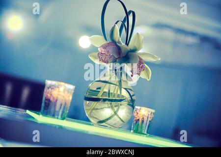 Beautiful orchid cocktail flower arrangement with candles on lucite table set up for a party Stock Photo