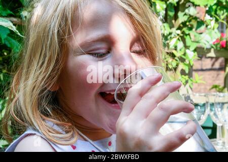 A seven year-old girl laughing while drinking water from a glass tumbler, London, UK Stock Photo