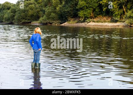 A thirteen year-old girl in wellington boots wading in the River Thames at Isleworth, London, UK Stock Photo