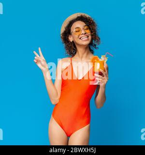 Summer Bliss. Funky Afro Girl In Swimsuit Enjoying Cocktail And Gesturing Peace Stock Photo