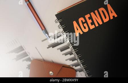 Word Agenda written on notebook over black background. Top view of copybook, pen and wallet. Business concept Stock Photo