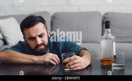Ruined life with alcohol. Man sits at table and looks at glass in his hand Stock Photo