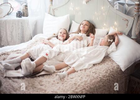 Three sisters in the bedroom in the morning. Girls in pajamas on the bed. Stock Photo