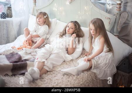 Three sisters in the bedroom in the morning. Girls in pajamas on the bed. Stock Photo