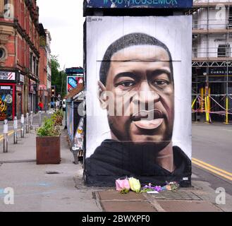 Flowers have been left at a mural depicting George Floyd, painted by street artist Akse, which has recently appeared in Stevenson Square, central Manchester, England, United Kingdom. Floyd, an African-American man, died in Minneapolis, Minnesota, United States, on May 25, 2020, while being arrested by 4 police officers after a shop assistant alleged he tried to pay with a counterfeit $20 bill. Stock Photo