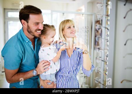Happy mother and father choosing eyeglasses frame with their daughter in optical store Stock Photo