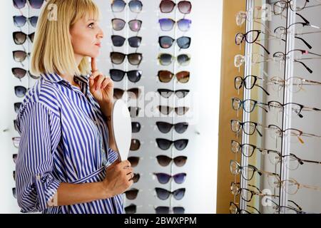 Pretty young woman is choosing new glasses at optics store Stock Photo