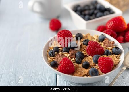Granola with blueberries and raspberries in white bowl on dark white desk. Stock Photo