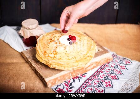 Woman puts berries on pancakes with cream, hands closeup, home cooking.  Stock Photo